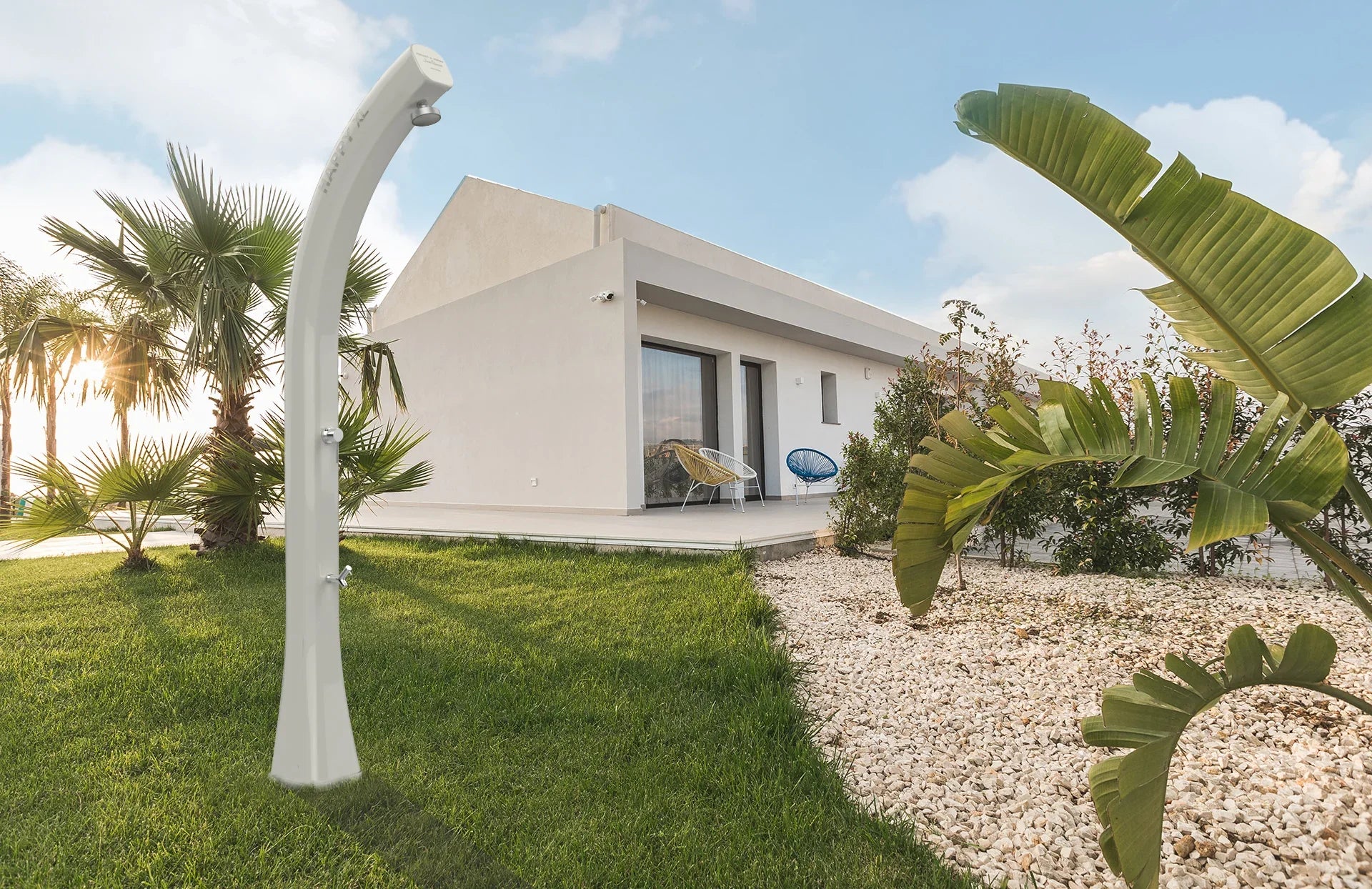 Doccia solare da giardino in acciaio davanti a casa moderna con prato e palme