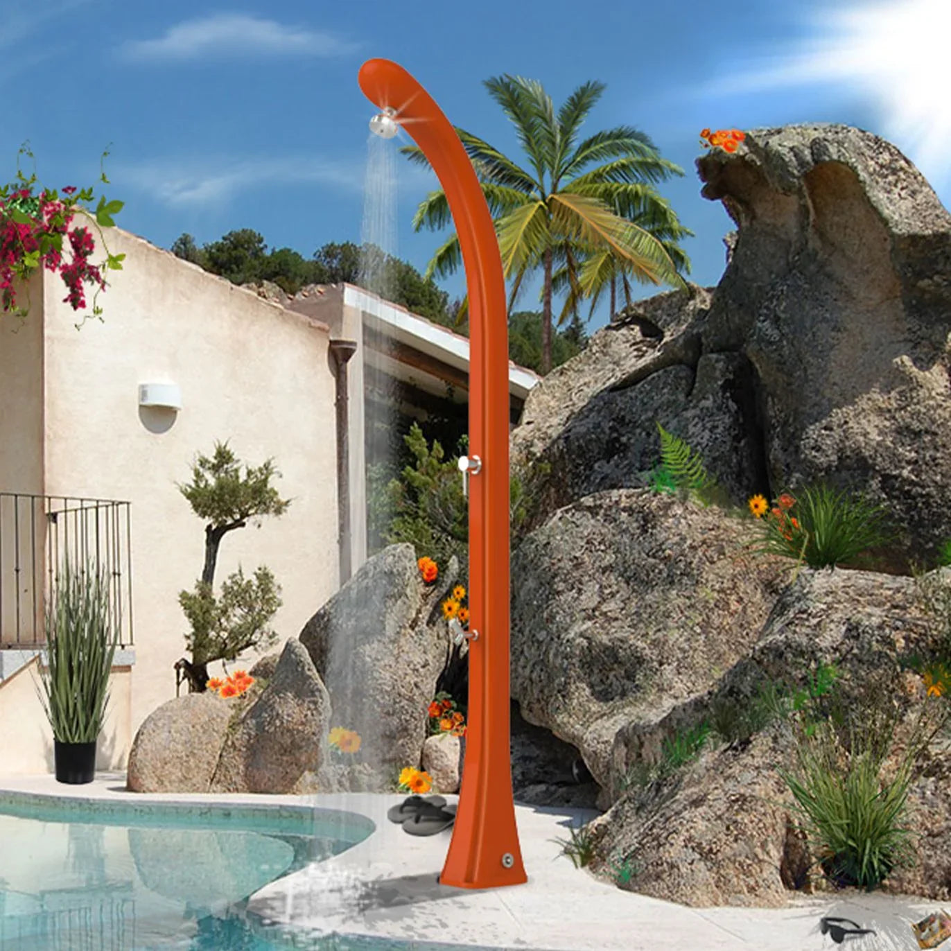 Doccia solare arancione da esterno vicino piscina, ambiente giardino con rocce e palme